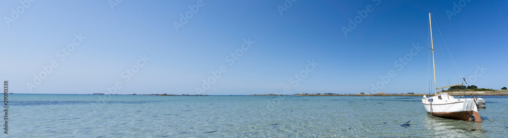 very wide panorama ocean coast and beach landscape with small sailboat under a blue sky