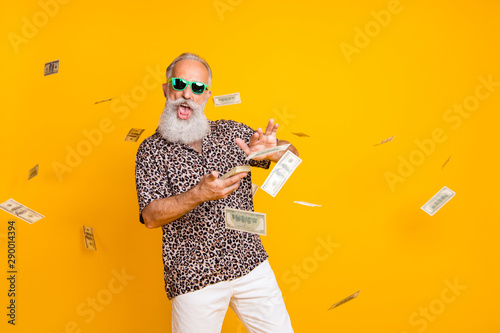 Portrait of crazy funny funky old long bearded man millionaire in eyewear eyeglasses waste money throw banknotes wear leopard shirt shorts isolated over yellow background photo