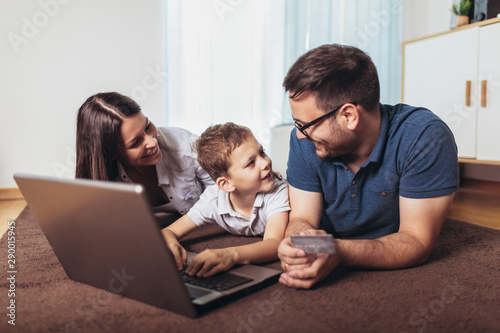 Beautiful parents and their son are doing shopping online using laptop and smiling at home.
