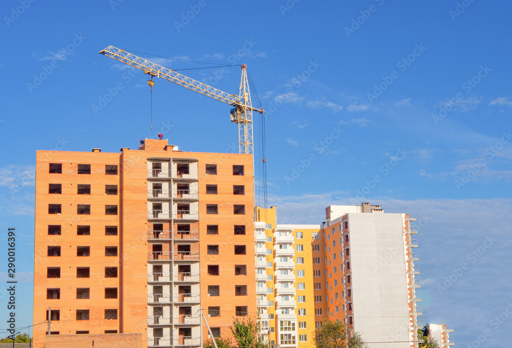 Brick multistory building under construction with crane on the site, new condominium on background