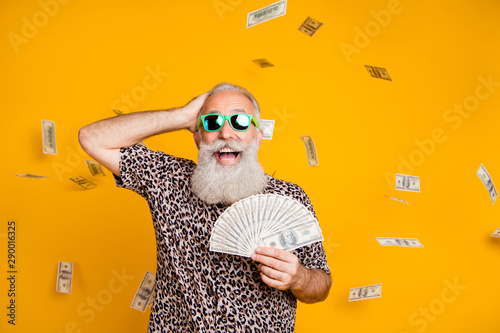 Portrait of retired old funny bearded man in eyewear eyeglasses scream omg look at falling money win lottery wearing leopard t-shirt isolated over yellow background photo