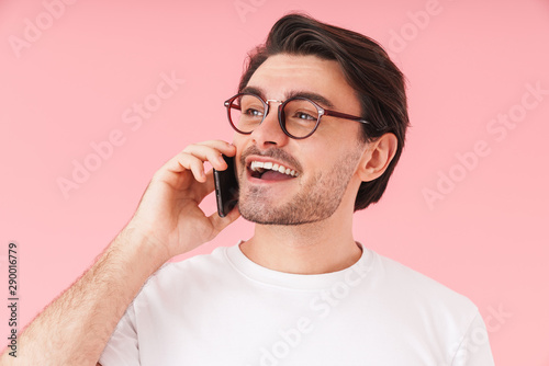 Image of young satisfied man wearing eyeglasses talking on cellphone and smiling