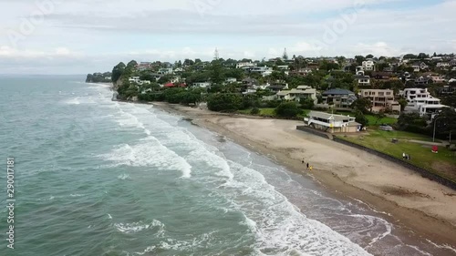 Aerial wide orbit over Mairangi Bay ocean waves & suburban waterfront community properties along the coast, Auckland, New Zealand photo