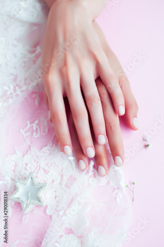 woman hands with manicure among white lace on pink background, cosmetic concept