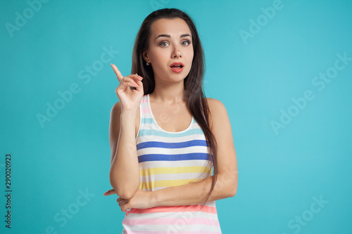 Brunette woman with long hair, dressed in colorful striped shirt, posing against blue studio background. Sincere emotions. Close-up.