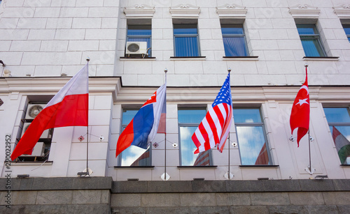 Waved national flags on facade wall with windows. Government or business building of some international organization or company. Flags of Poland, Slovakia, USA and Turkey