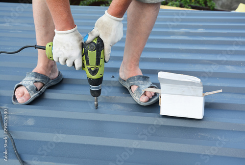 Roofer with screw gun installing lightweight metal roof tiles roofing construction