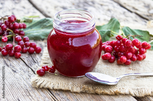 Viburnum fruit jam in a glass jar on a wooden table near the ripe red viburnum berries. Source of natural vitamins. Used in folk medicine. photo