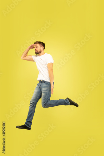 Full length portrait of happy jumping man isolated on yellow background. Caucasian male model in casual clothes. Freedom of choices, inspiration, human emotions concept. Run for sales, hurry up. © master1305