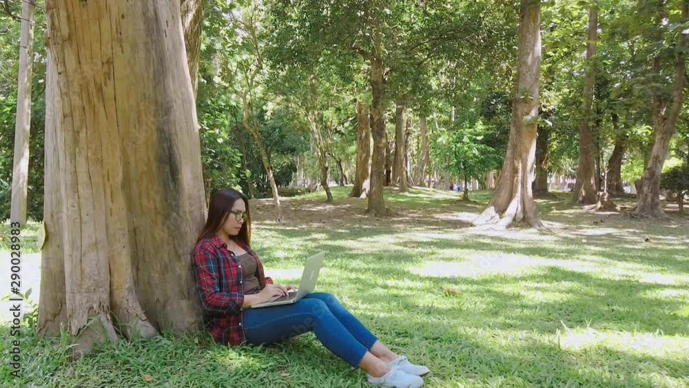 Business Asian woman using laptop working typing on laptop keyboard and sitting in the park on green grass in outdoor. Is not in focus or focus is too soft. Business Asian woman using laptop working typing on laptop keyboard and sitting in the park on green grass in outdoor. Is not in focus or focus is too soft.