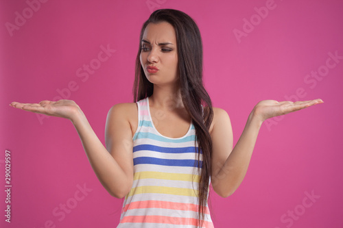 Brunette woman with long hair, dressed in colorful striped shirt, posing against pink studio background. Sincere emotions. Close-up.