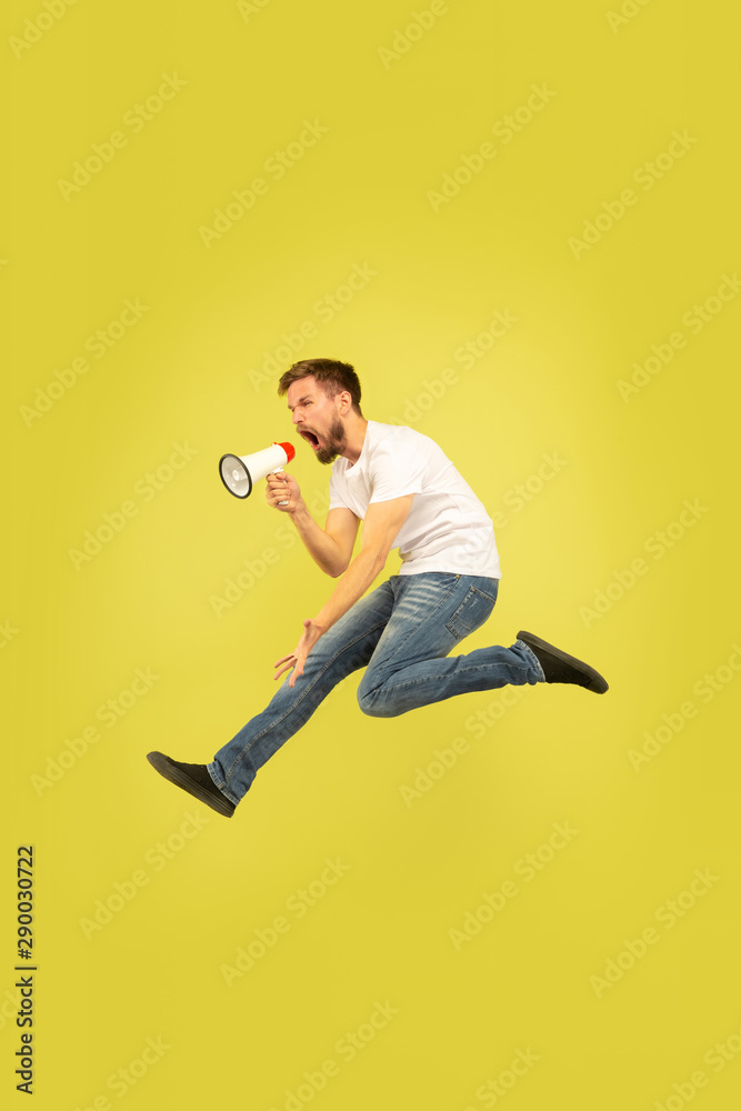Full length portrait of happy jumping man isolated on yellow background. Caucasian male model in casual clothes. Freedom of choices, inspiration, human emotions concept. Calling with mouthpeace. Full length portrait of happy jumping man isolated on yellow background. Caucasian male model in casual clothes. Freedom of choices, inspiration, human emotions concept. Calling with mouthpeace.