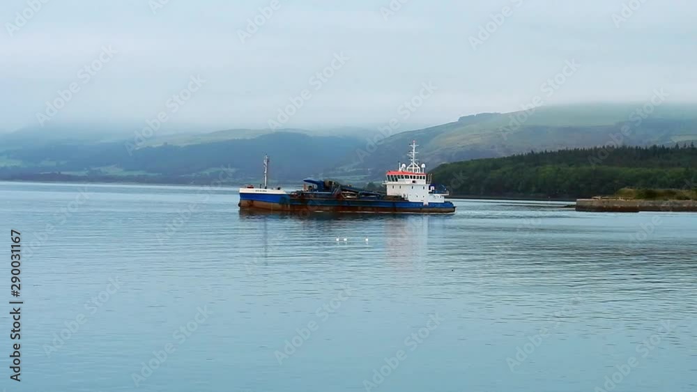 Commercial fishing trawler boat heading out of English North Wales harbour seascape on calm sea reflections. Commercial fishing trawler boat heading out of English North Wales harbour seascape on calm sea reflections.