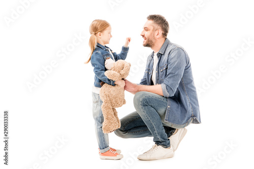 side view of daughter with teddy bear and bearded dad looking at each other isolated on white