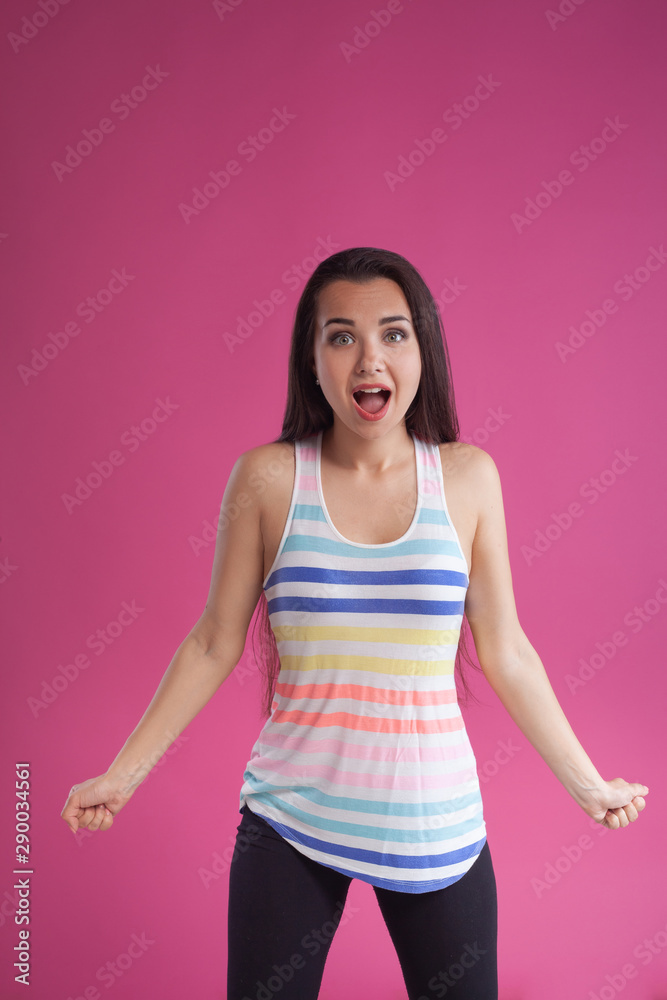 Brunette woman with long hair, dressed in colorful striped shirt, posing against pink studio background. Sincere emotions. Close-up. Brunette woman with long hair, dressed in colorful striped shirt, posing against pink studio background. Sincere emotions. Close-up.