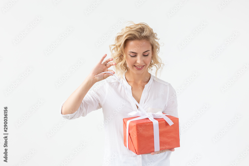 Cheerful good looking young blond woman holding a red gift box in her hands, but against a white background. Concept holidays and presents Cheerful good looking young blond woman holding a red gift box in her hands, but against a white background. Concept holidays and presents