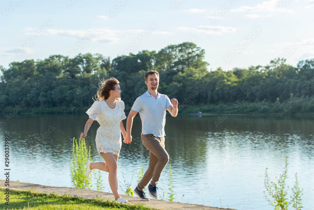 Summer nature, relationship and people in love concept - happy couple running near the lake Summer nature, relationship and people in love concept - happy couple running near the lake