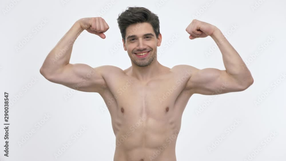 Smiling young brunette man with naked torso showing his biceps and kissing them while looking at the camera over white background isolated Smiling young brunette man with naked torso showing his biceps and kissing them while looking at the camera over white background isolated