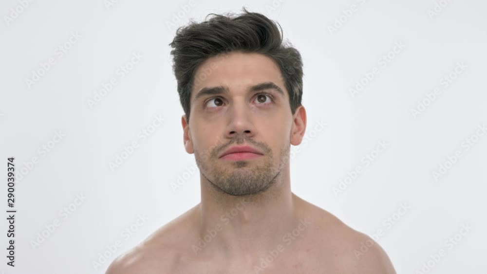 Close up view of young brunette man with naked torso looking up with crossed eyes and fixing his hairstyle with hand over white background isolated Close up view of young brunette man with naked torso looking up with crossed eyes and fixing his hairstyle with hand over white background isolated