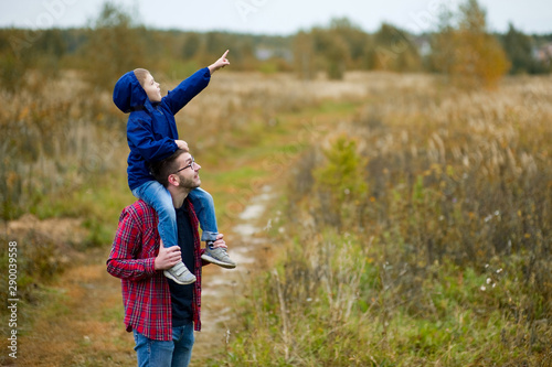 The son sits on his father s shoulders and points to the sky. Toned