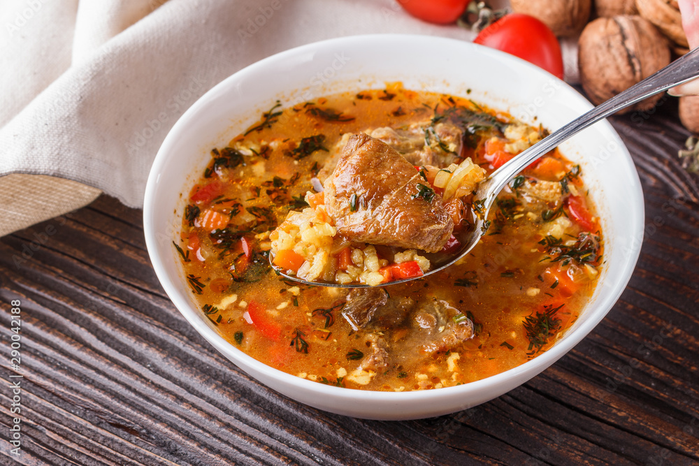 Georgian soup. Kharcho with rice, tomato, beef, garlic and herbs in bowl on wooden table