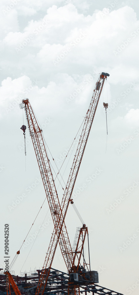 Boom cranes at a construction site against the sky and clouds. Vertical rectangular image.