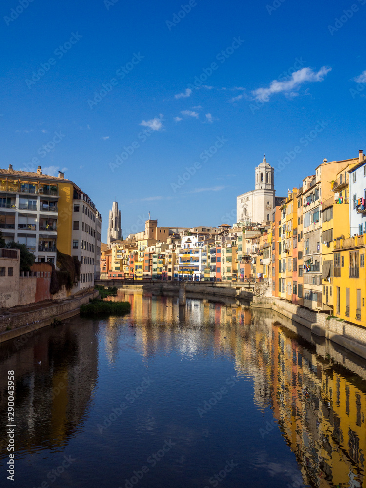 Girona's tipical skyline cityscape over the Onyar River with colourful river houses on a blue sunny sky, Church of Sant Feliu Cathedral landmark on background