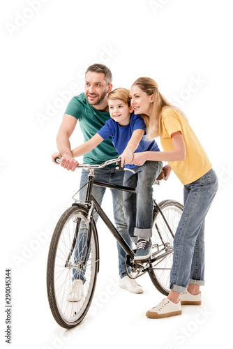 full length view of smiling parents teaching son to ride bike isolated on white