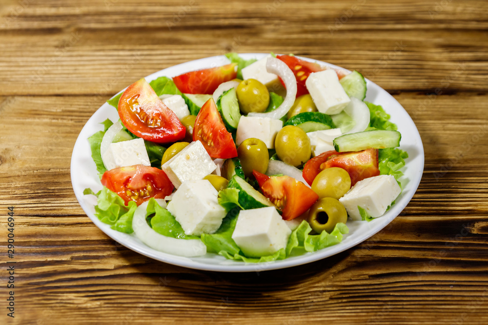 Greek salad with fresh vegetables, feta cheese and green olives on wooden table