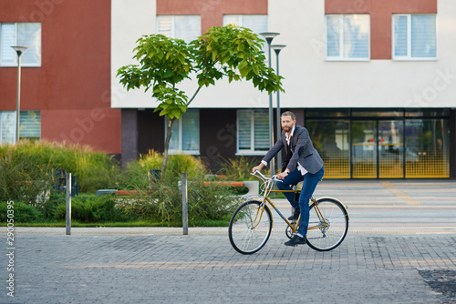 Bearded Businessman in business suit riding on retro bicycle to work on urban street in the morning on sunset