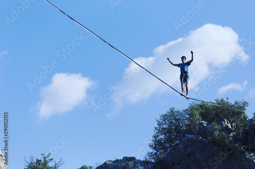 A man is walking along a stretched sling. Highline in the mountains. Man catches balance. Performance of a tightrope walker in nature. Highliner on the background of the mountains.
