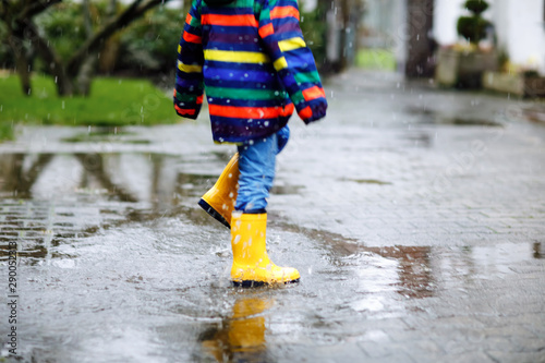 Close-up of kid wearing yellow rain boots and walking during sleet, rain and snow on cold day. Child in colorful fashion casual clothes jumping in a puddle. Having fun outdoors