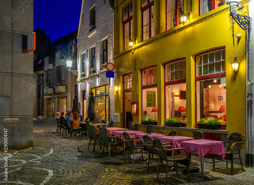 Old street with tables of cafe in Bruges (Brugge), Belgium. Night cityscape of Bruges. Typical architecture of Bruges