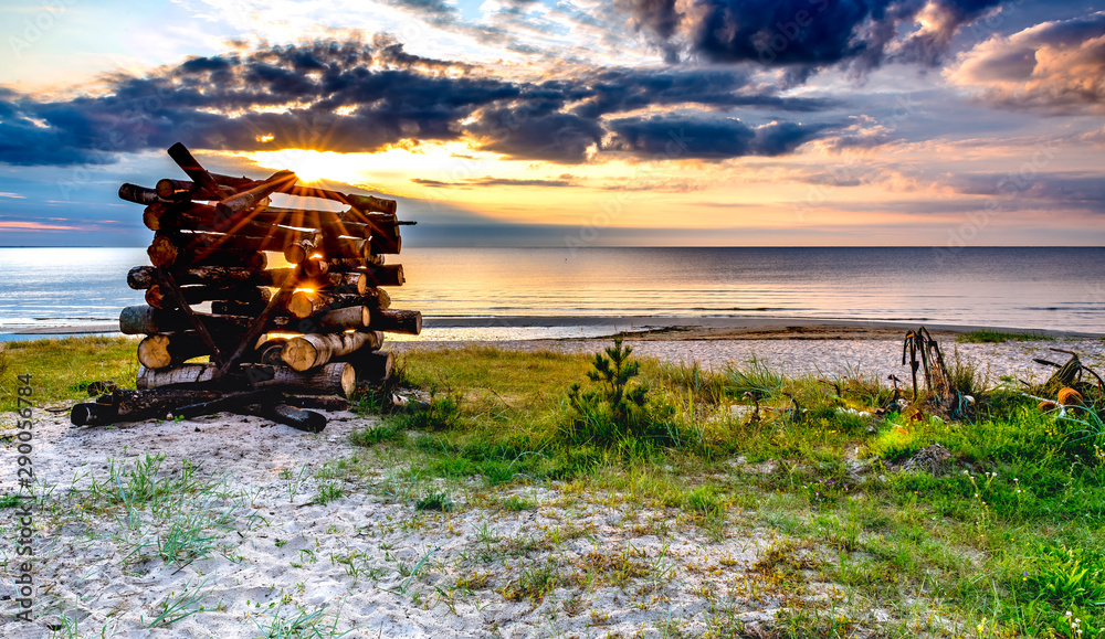 Fototapeta premium Coastal landscape with pile of wood and fishing anchors on sandy beach of the Baltic sea at dawn