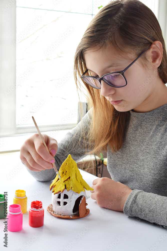 Girl making toys with your own hands paints a clay house with gouache. Indoors creative leisure for children. Supporting creativity learning by doing DIY project hand craft. Master class of art Stock ...