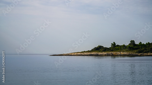 Fototapeta Naklejka Na Ścianę i Meble -  An early morning, the sky covered with clouds merges with the sea on the horizon. View of a stony forested coast