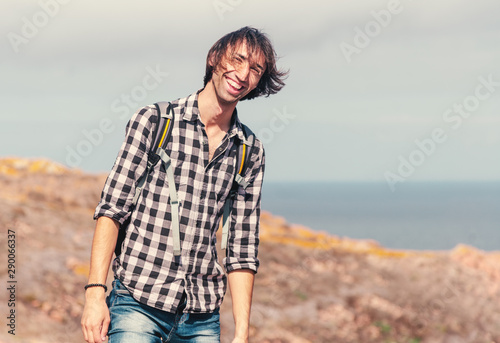 Portrait of a happy young man on a hill against the background of the sea on a journey, walking outdoor