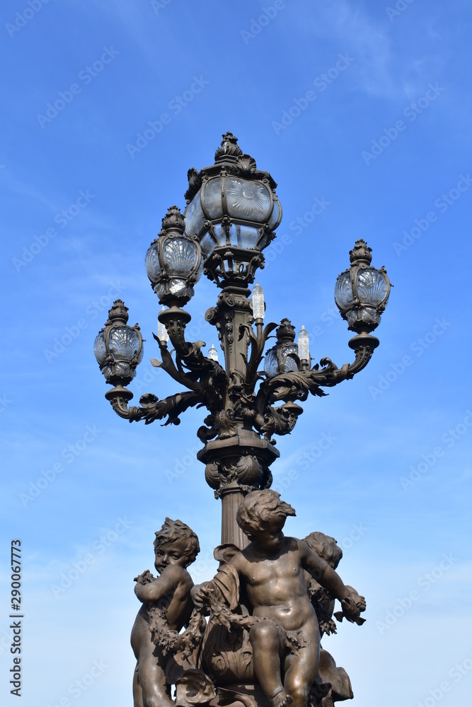 Pont Alexandre III detail, bronze streetlight with sculptures and blue sky. Paris, France.