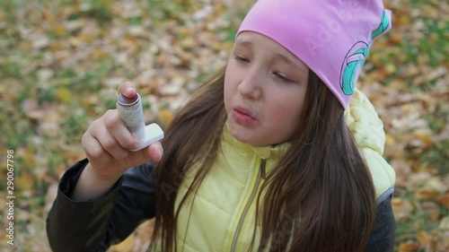 A girl in a hat and jacket takes medicine in the form of an inhaler for bronchial asthma in the autumn forest during a walk. Flu season and cold rhinitis. Allergic kid. Sick kids. photo