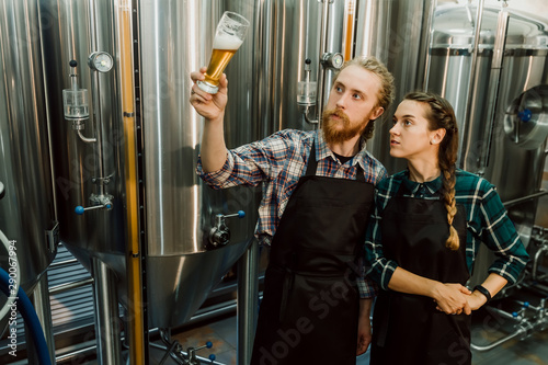Canvas Print Brewery workers looking at freshly made beer in glass tube and discussing it
