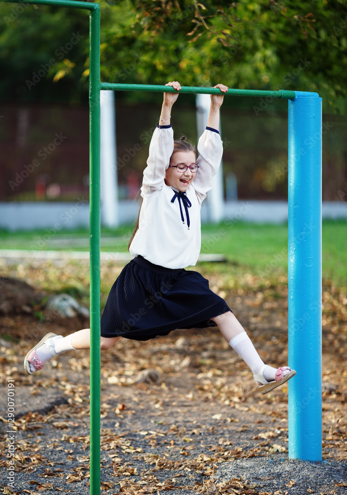 Happy schoolgirl hangs on the horizontal bar. Child girl having fun on the playground. Vertical shot. Selective focus. Happy schoolgirl hangs on the horizontal bar. Child girl having fun on the playground. Vertical shot. Selective focus.