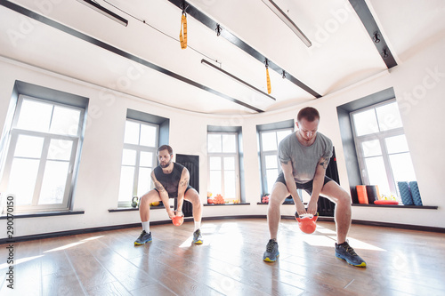 Young strong male friends train with weights in the gym equipped with the trx system. The concept of joint training and the pursuit of a common goal
