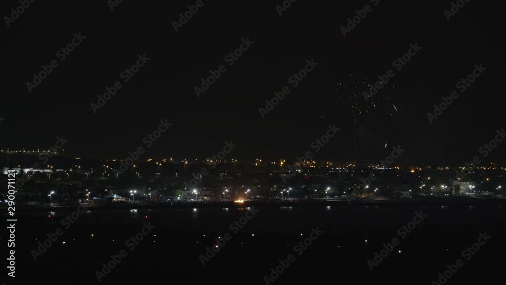 A pitch black night urban view with multiple streetlights here and there. The bright firework is sparkling over it, being reflected in the nearby water A pitch black night urban view with multiple streetlights here and there. The bright firework is sparkling over it, being reflected in the nearby water