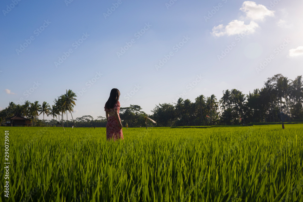  natural lifestyle portrait of young beautiful and happy Asian Chinese woman in elegant Summer dress walking carefree and relaxed at fresh tropical rice field enjoying