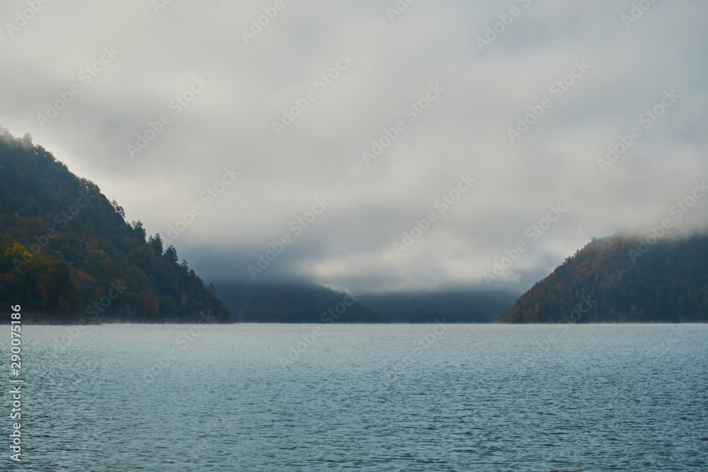 Lake in the midst of mountains and forests in fog autumn. Nature in Norway in autumn