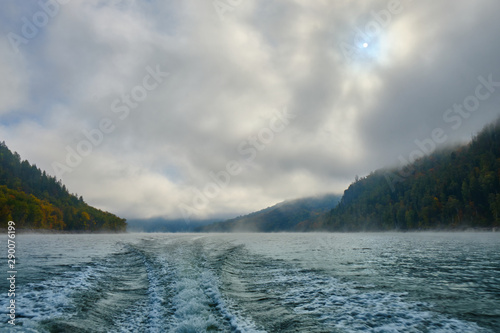 The trail of the boat (Wake) on a Norwegian lake in the middle of the mountains and fog in the autumn. Boat trip on the lake in autumn