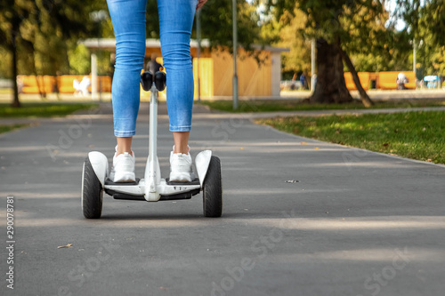 Legs of a girl in white sneakers on a white hoverboard, self-balancing scooter in a park close-up. Active lifestyle technology future copy space