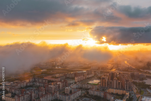 Urban cityscape, aerial top view with low flying clouds over a residential area of the city, view of the horizon and the dawn of the sun.