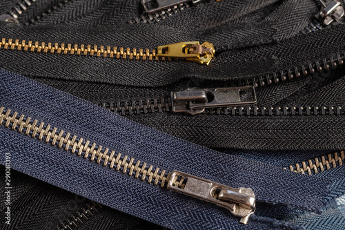 Pack a lot of black navy metal brass antique zippers stripes with sliders pattern for handmade sewing tailoring leathercraft on the blue wooden background