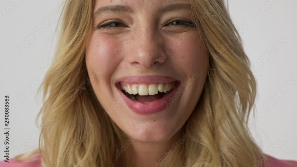 Cropped view of happy young blonde woman smiling and laughing while looking at the camera over gray background isolated Cropped view of happy young blonde woman smiling and laughing while looking at the camera over gray background isolated